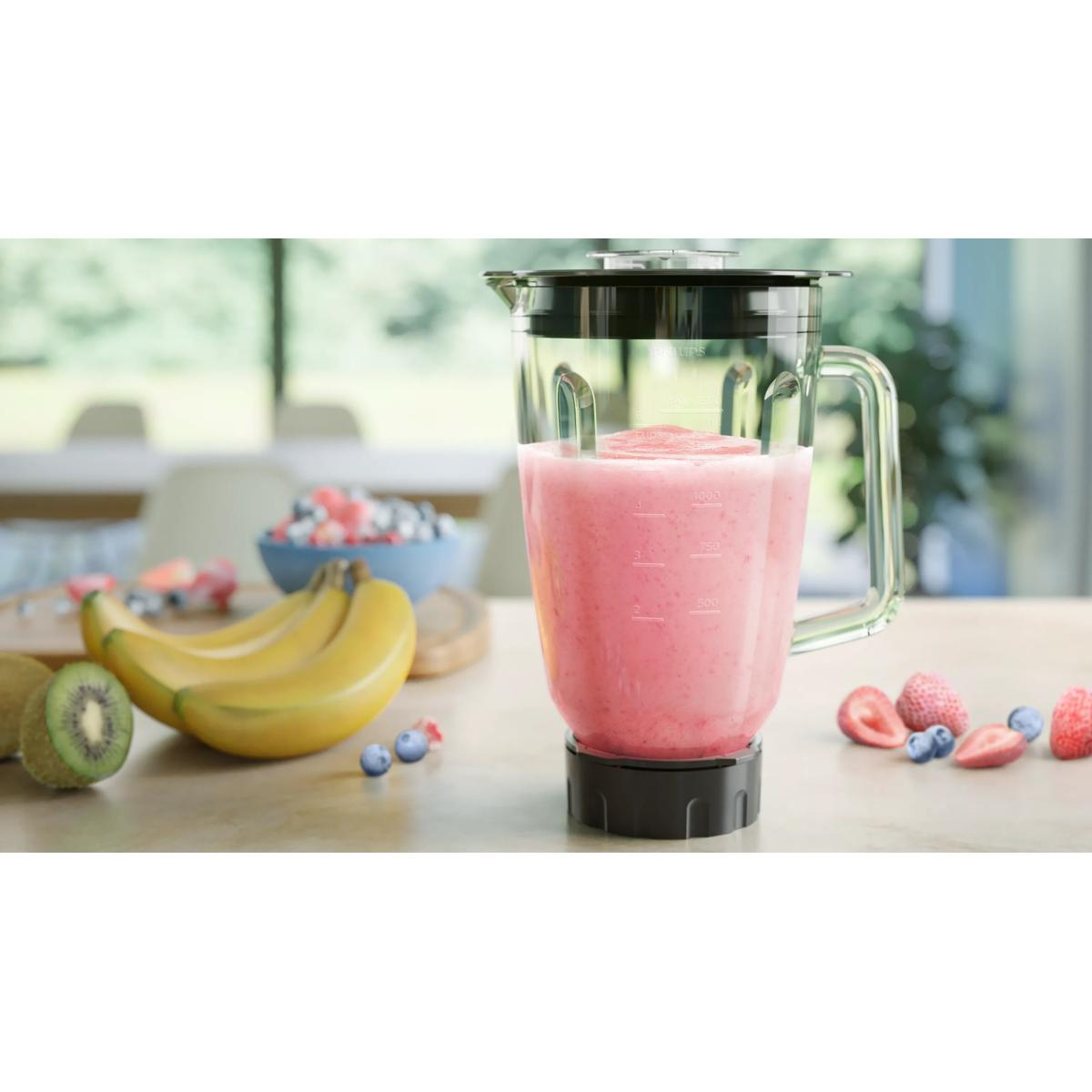 Ein Mixer mit rosa Smoothie, Bananen, Kiwi und Beeren auf einem Holztisch.