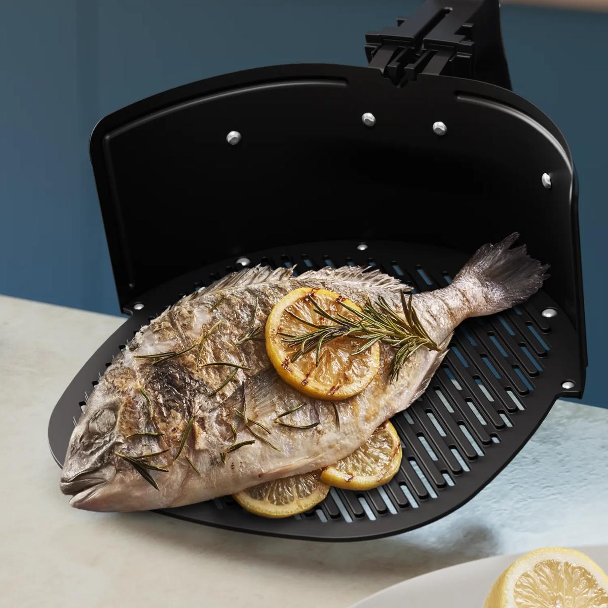 Ganze gegrillte Dorade mit Zitronenscheiben und Rosmarin im Airfryer Korb.