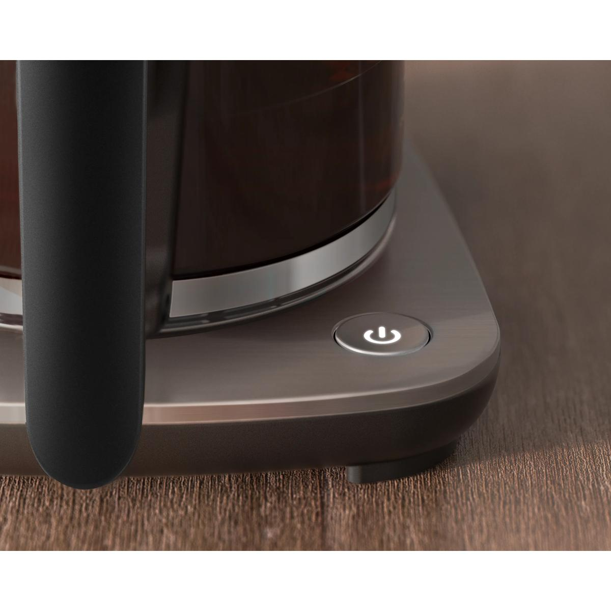 Podświetlony przycisk zasilania świeci na metalowej podstawie urządzenia ze szklanym dzbankiem.