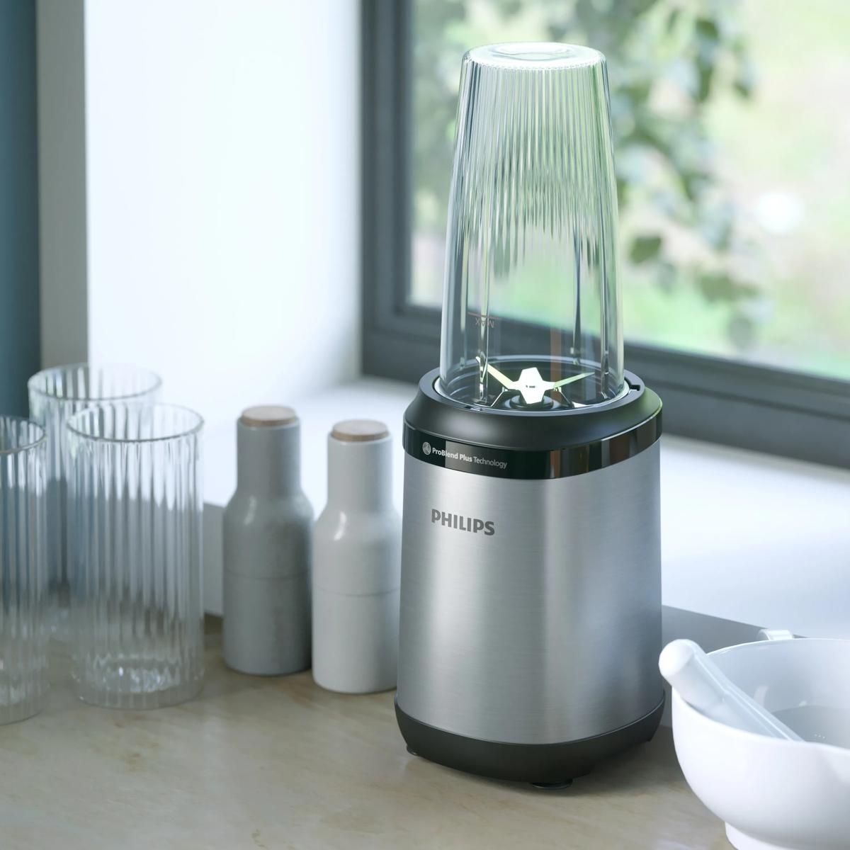 Srebrny blender Philips ze szklaną pokrywą stoi na blacie, obok szklanek i misek.