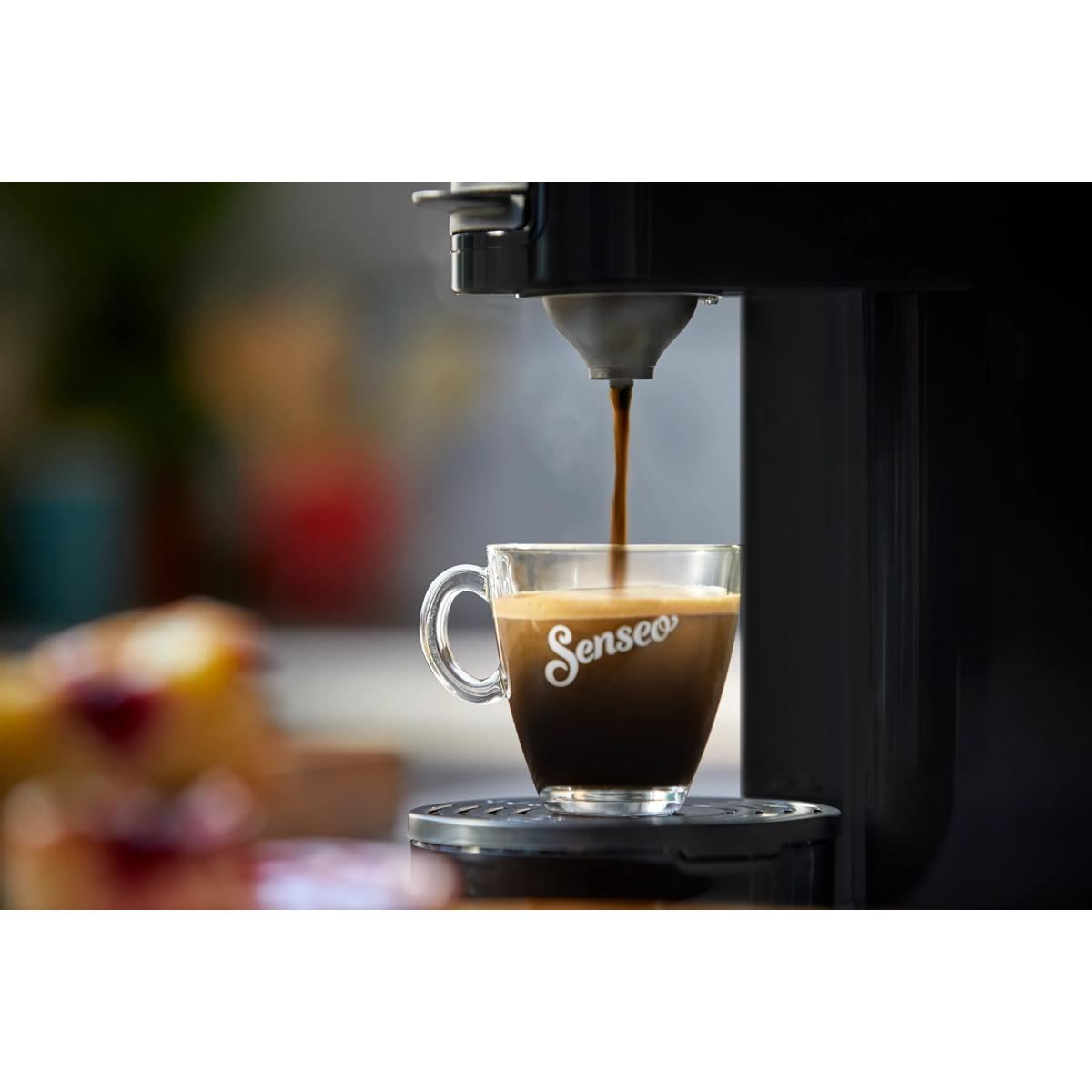 Kaffee fließt in eine Tasse, daneben ein Stück Kuchen.