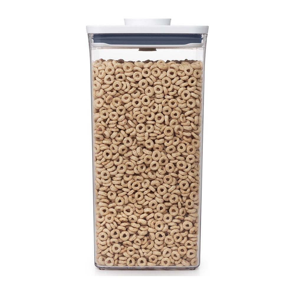 Un contenitore trasparente riempito di cereali marrone chiaro, coperchio bianco.