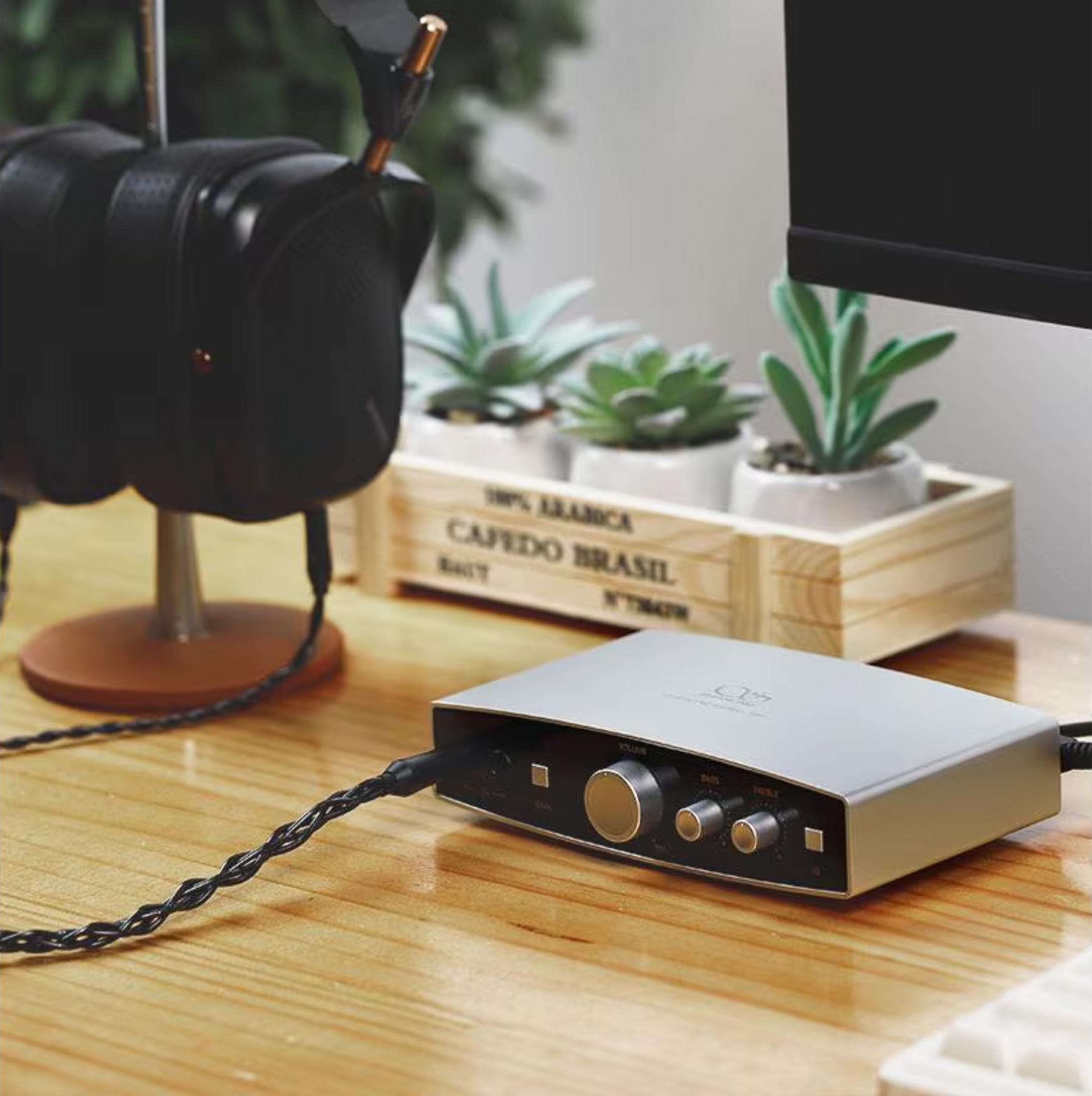 Una interfaz de audio plateada con perillas y botones se sienta sobre un escritorio de madera junto a auriculares.