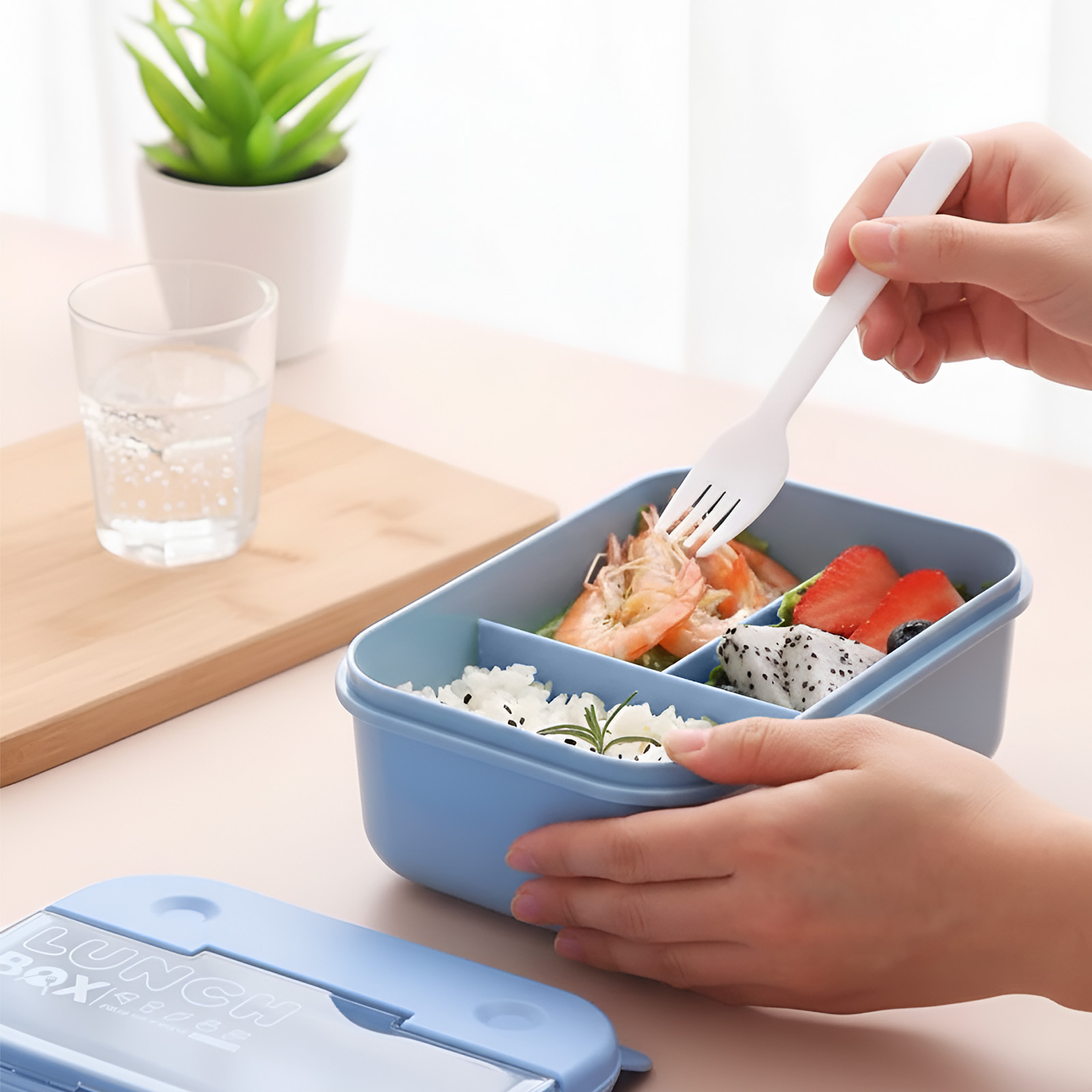 Una persona usa una forchetta per prendere gamberi da un portapranzo blu con riso e frutta.