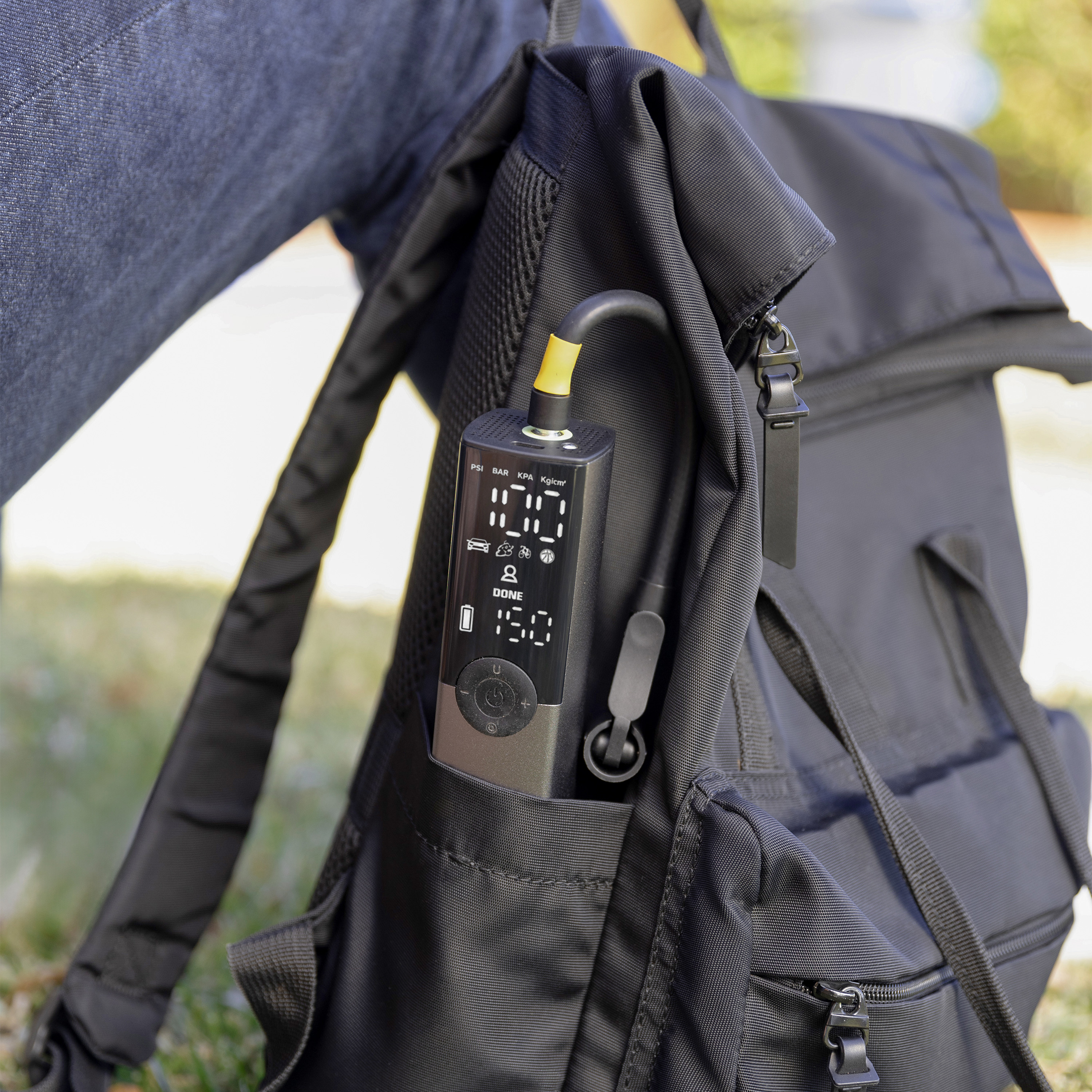 Ein tragbares Reifenfüllgerät mit digitaler Anzeige steckt in der Tasche eines schwarzen Rucksacks.