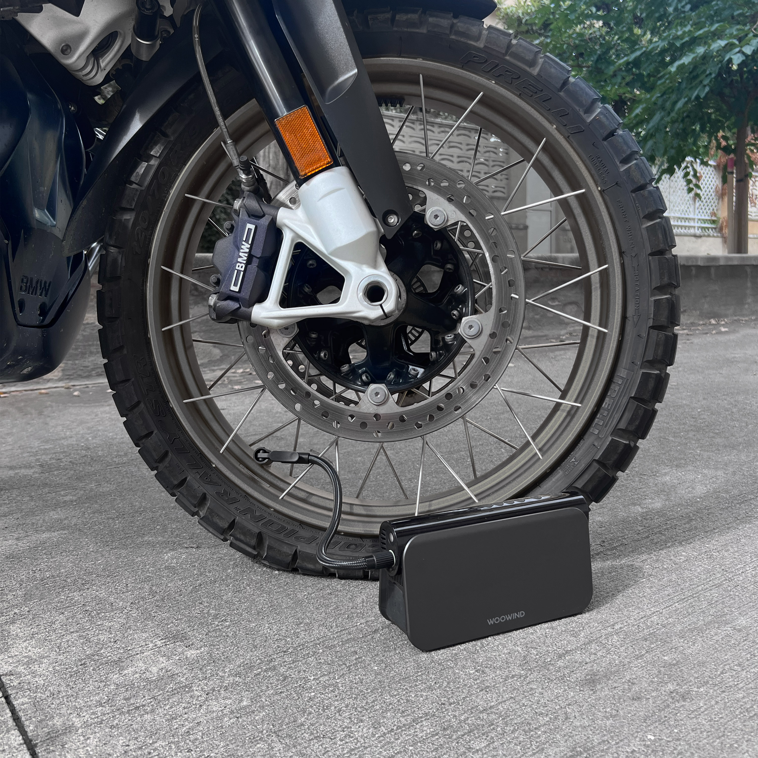 Un compresor de aire portátil negro junto a una rueda de moto en asfalto.