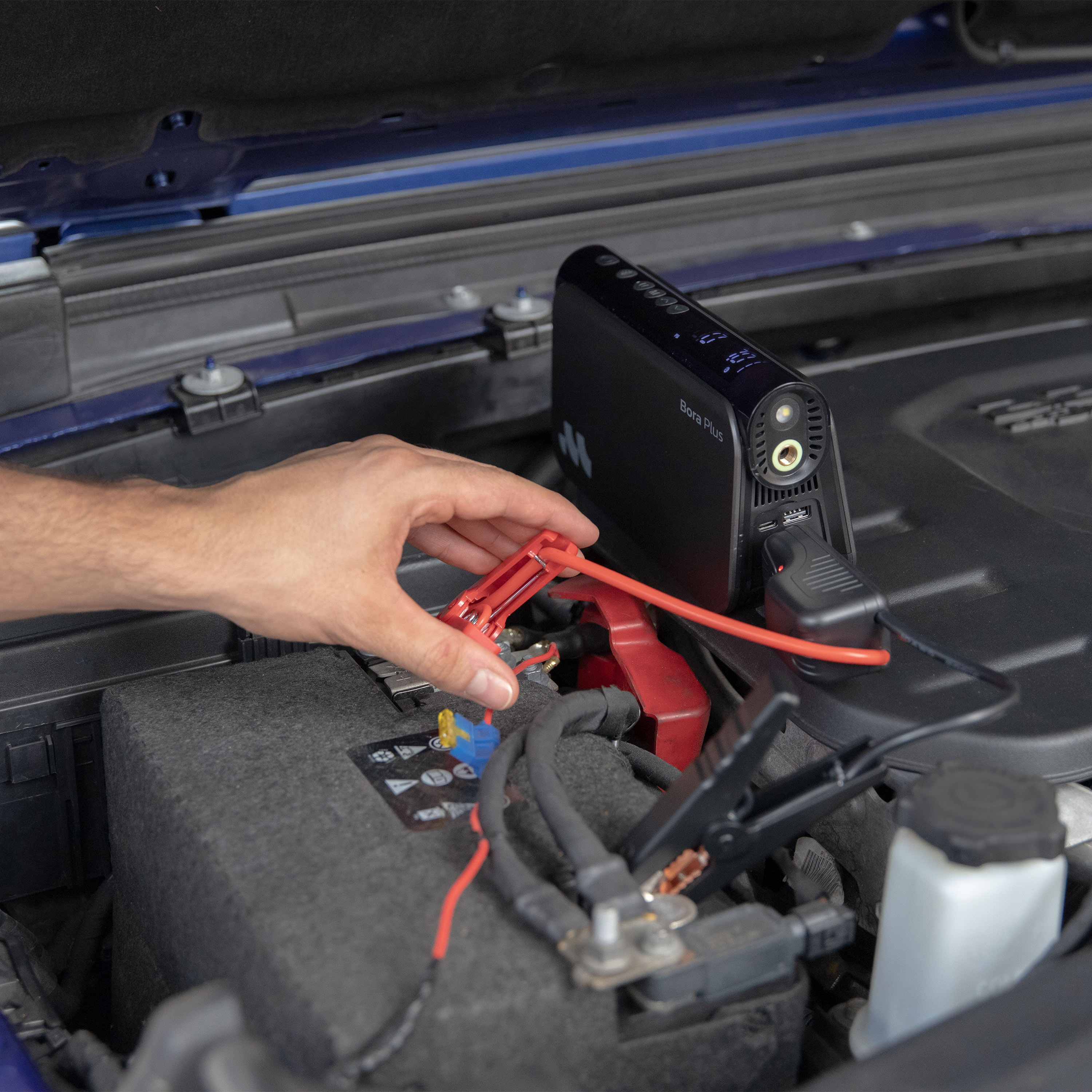 Uomo collega cavi di avviamento a batteria auto, con un avviatore nero accanto.