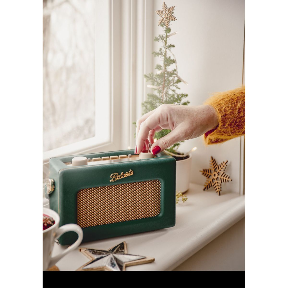 Eine Hand dreht an einem grünen Radio auf einem Fensterbrett mit Weihnachtsdeko.