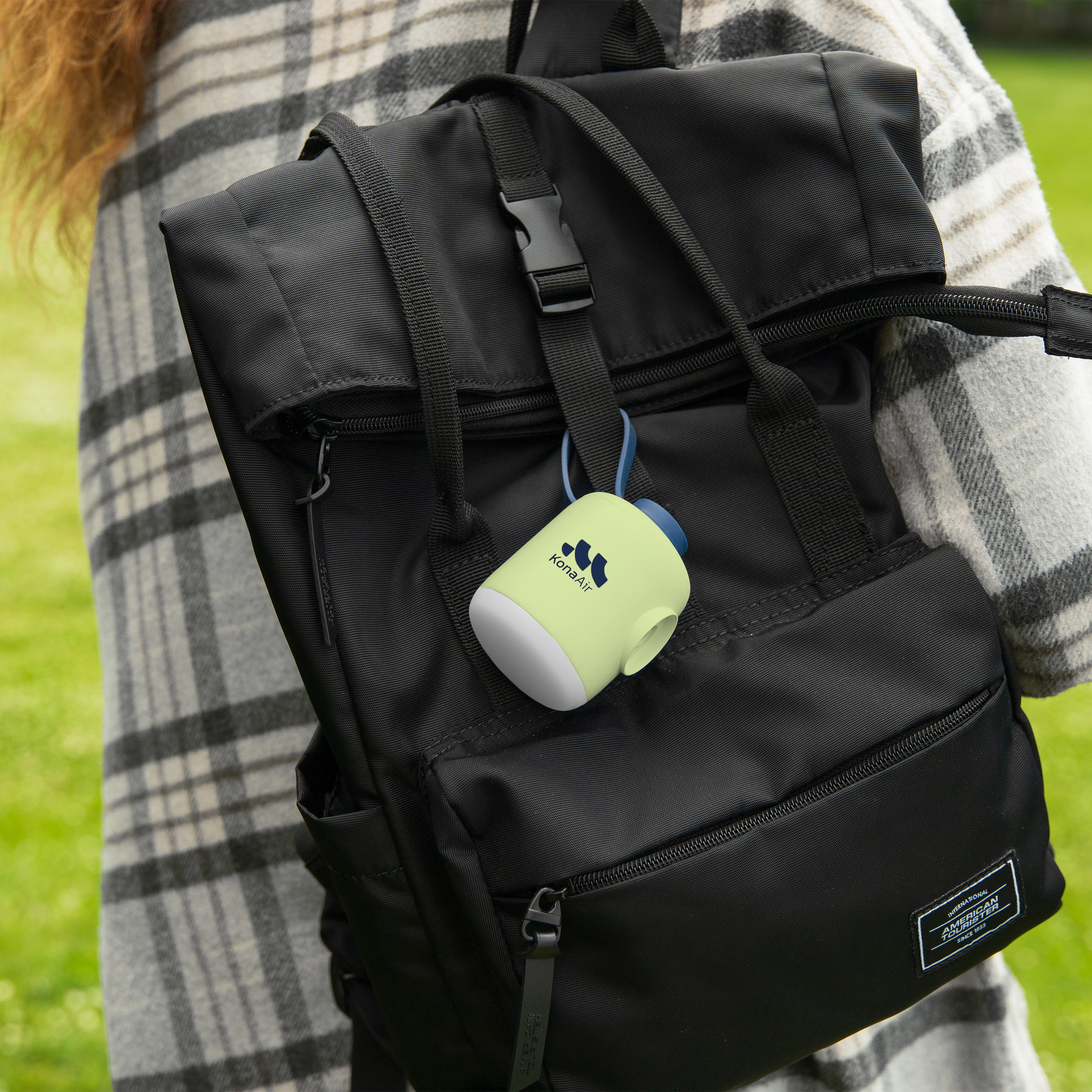 Una persona con bufanda a cuadros lleva una mochila negra con un accesorio amarillo.