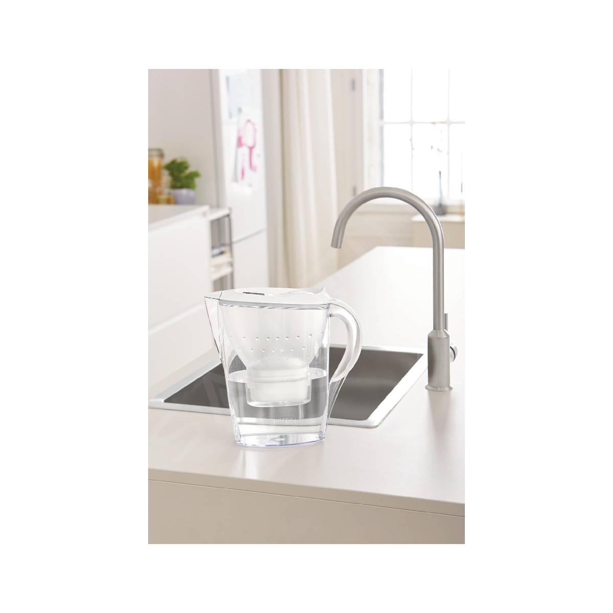 Przezroczysty dzbanek filtrujący wodę stoi na blacie kuchennym obok kranu.