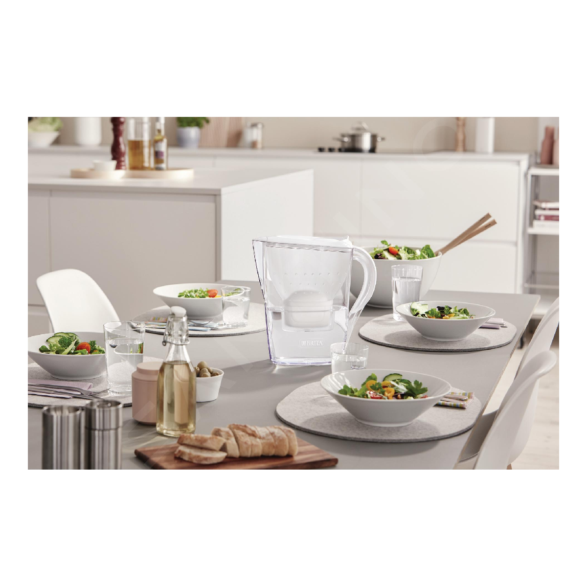 Stół nakryty sałatkami, chlebem, oliwą z oliwek i filtrem do wody.