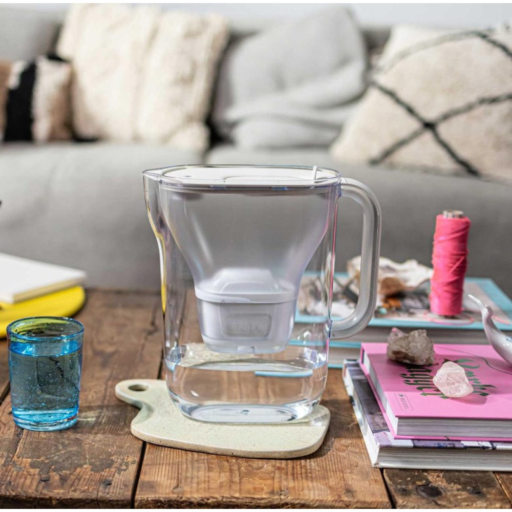 Dzbanek z filtrem do wody Brita stoi na drewnianym stole obok szklanki z wodą.