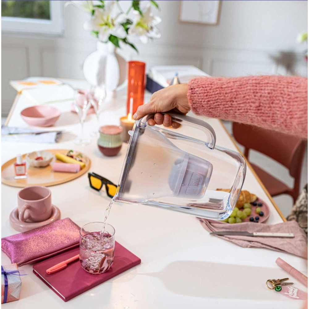 Ręka nalewa wodę z dzbanka do szklanki na stole z przekąskami.