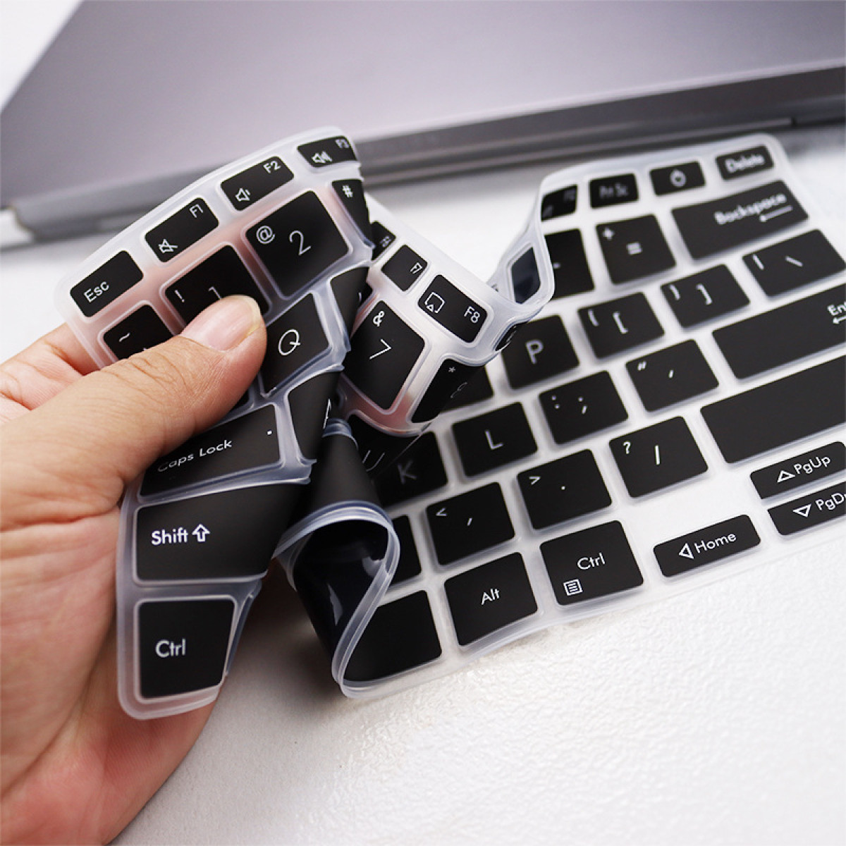 Eine Hand hält eine schwarze Tastaturabdeckung mit weißen Buchstaben über einem Laptop.