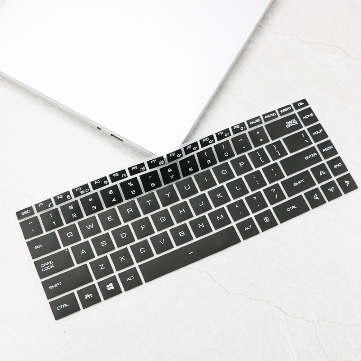 Eine schwarze Tastaturabdeckung mit weißen Buchstaben und Symbolen liegt auf einem weißen Laptop.