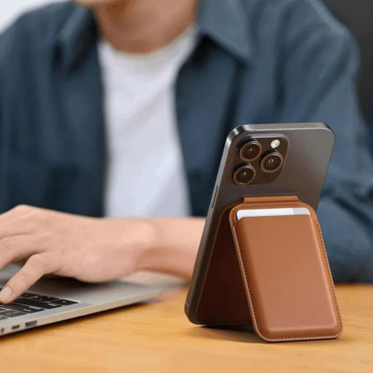 Una persona digita su un laptop accanto a uno smartphone con un portafoglio in pelle marrone.