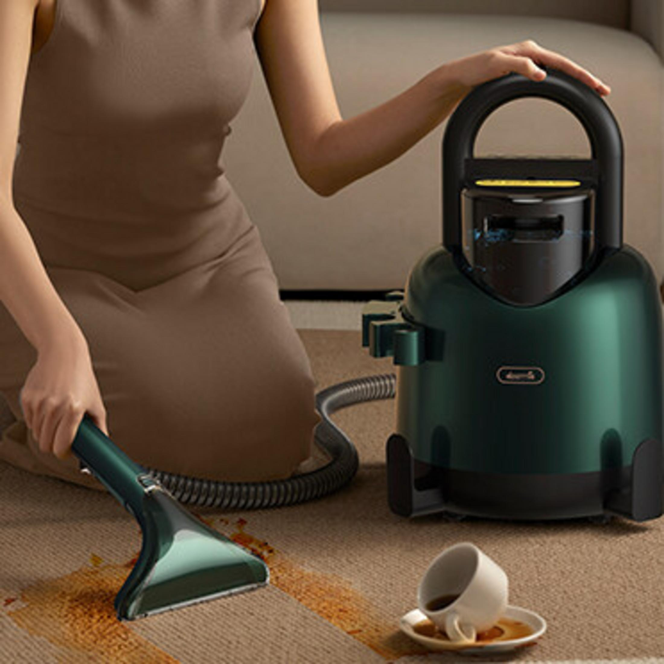 Una persona pulisce una macchia sul tappeto con un pulitore portatile accanto a una tazza di caffè rovesciata.