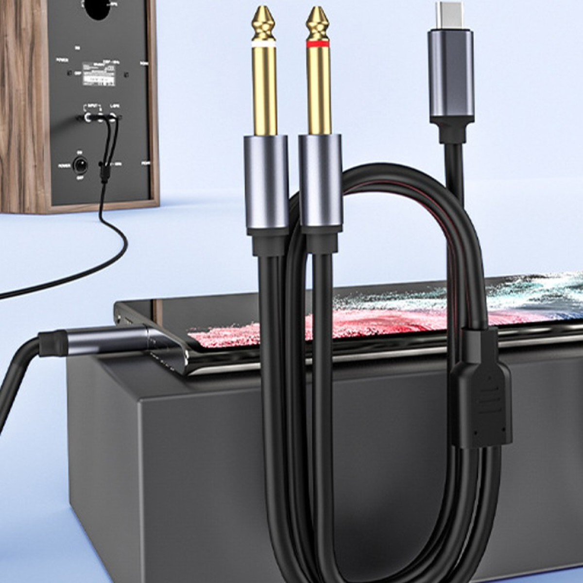 Kable audio ze złotymi wtykami i złączem USB-C przy głośniku i telefonie.