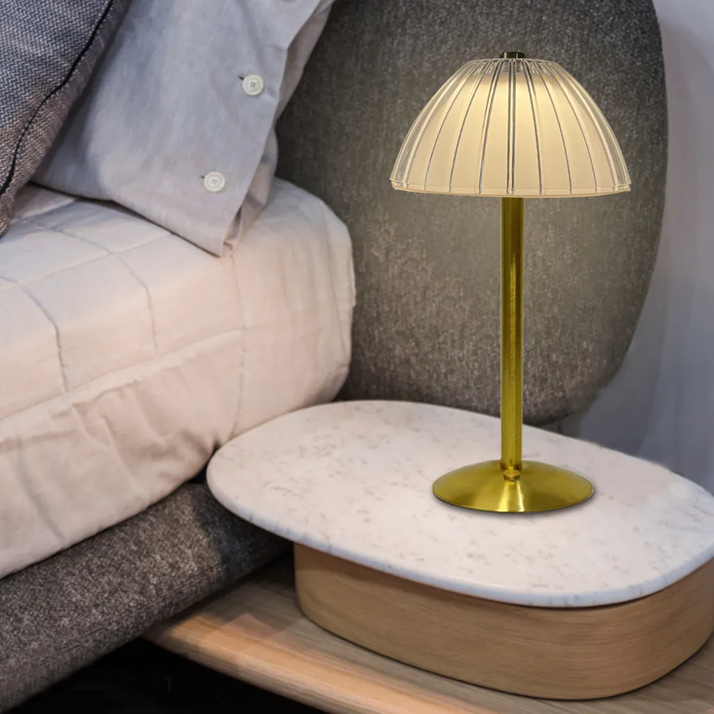 Eine goldene Lampe mit geripptem Schirm steht auf einem Nachttisch neben einem Bett.
