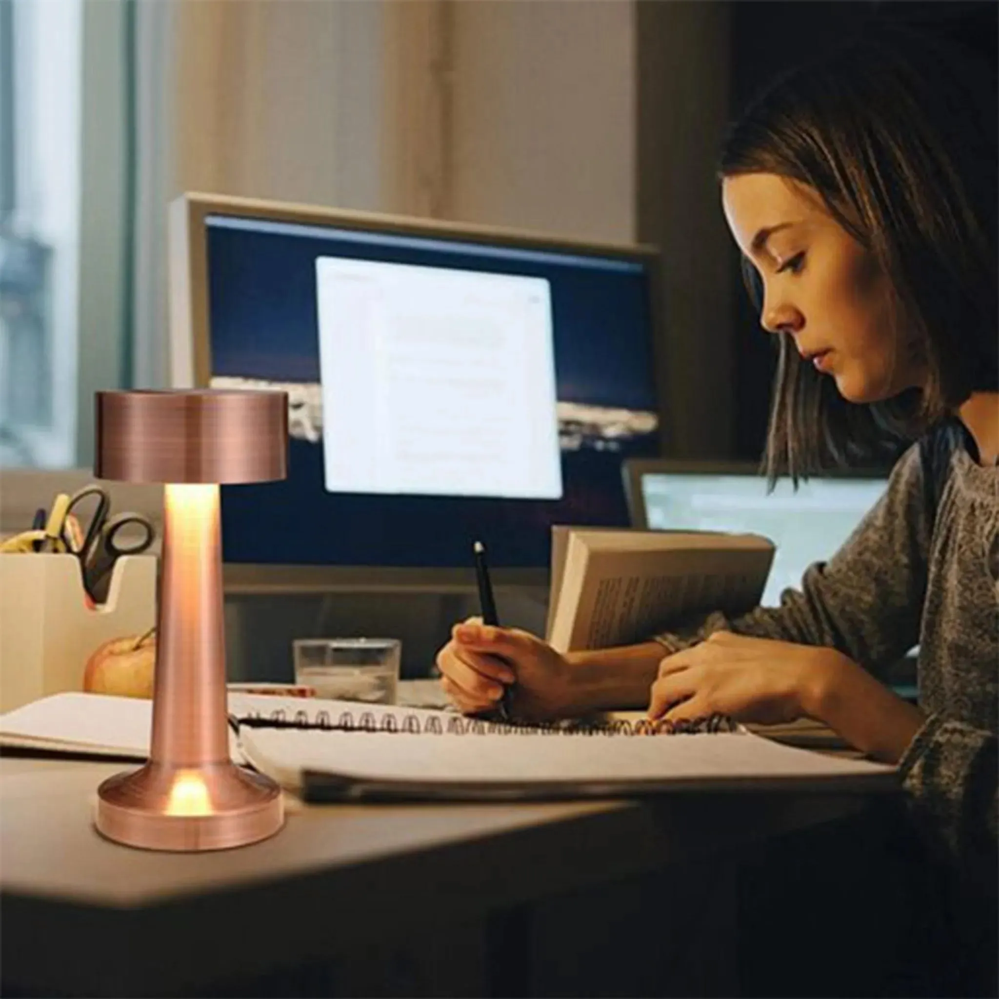 Eine junge Frau schreibt in einem Notizbuch, beleuchtet von einer kupferfarbenen Tischlampe.