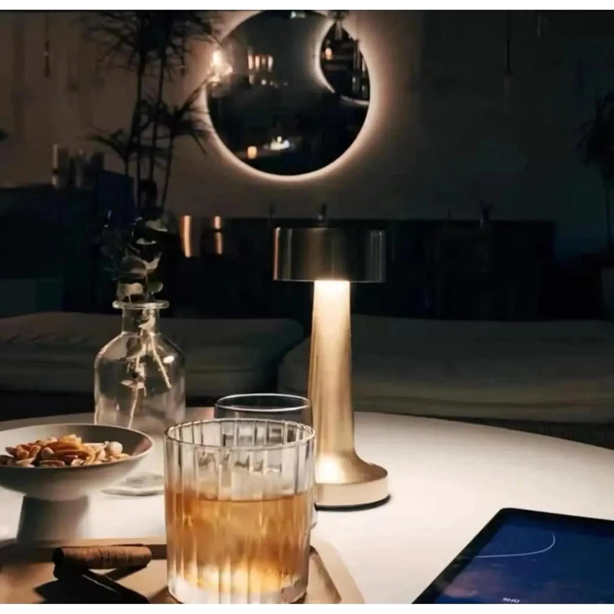 Ein goldenes Tischlicht beleuchtet eine Vase, ein Glas Whisky und eine Schüssel mit Nüssen.