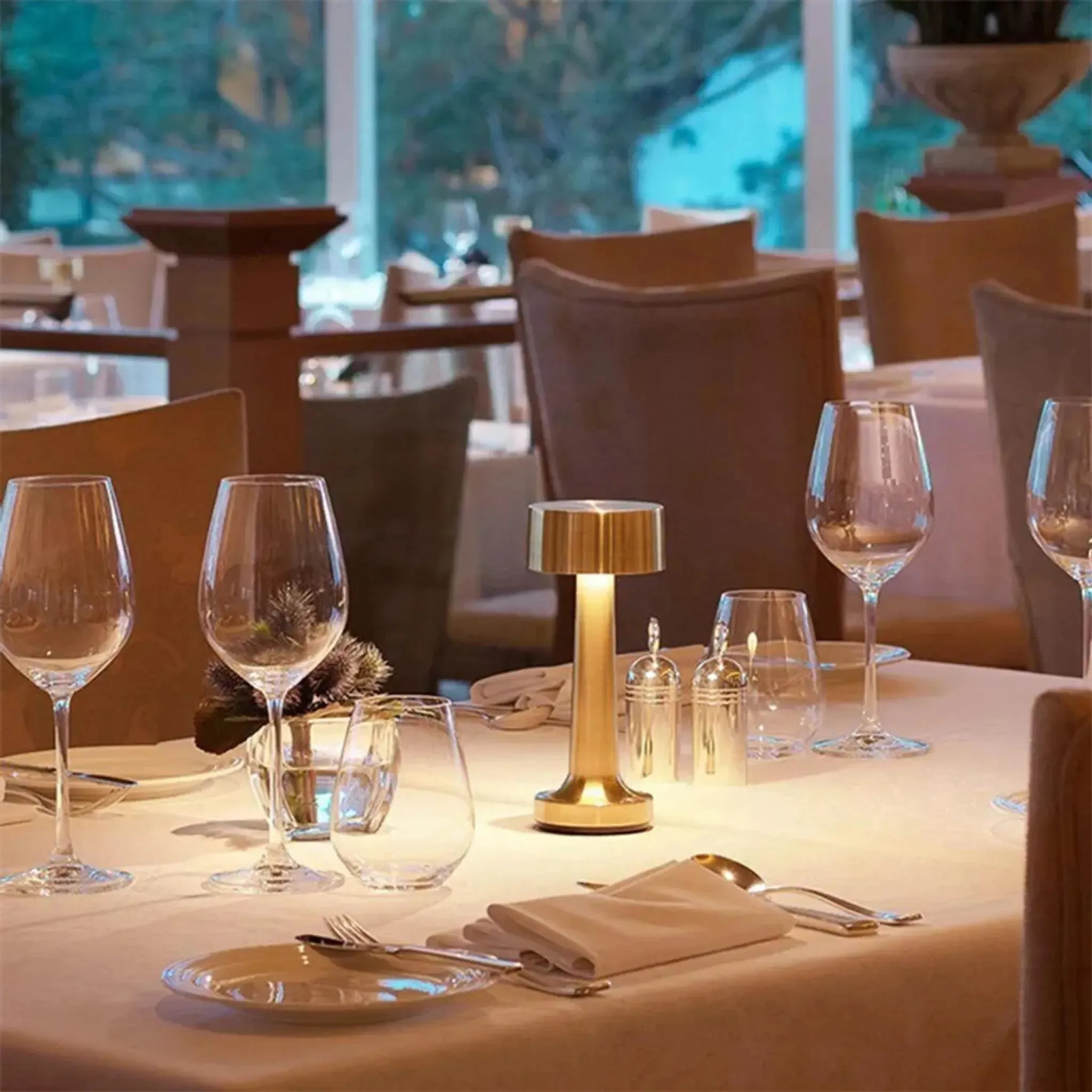 Ein Restauranttisch ist gedeckt mit Weingläsern, Besteck und einer goldenen Lampe.
