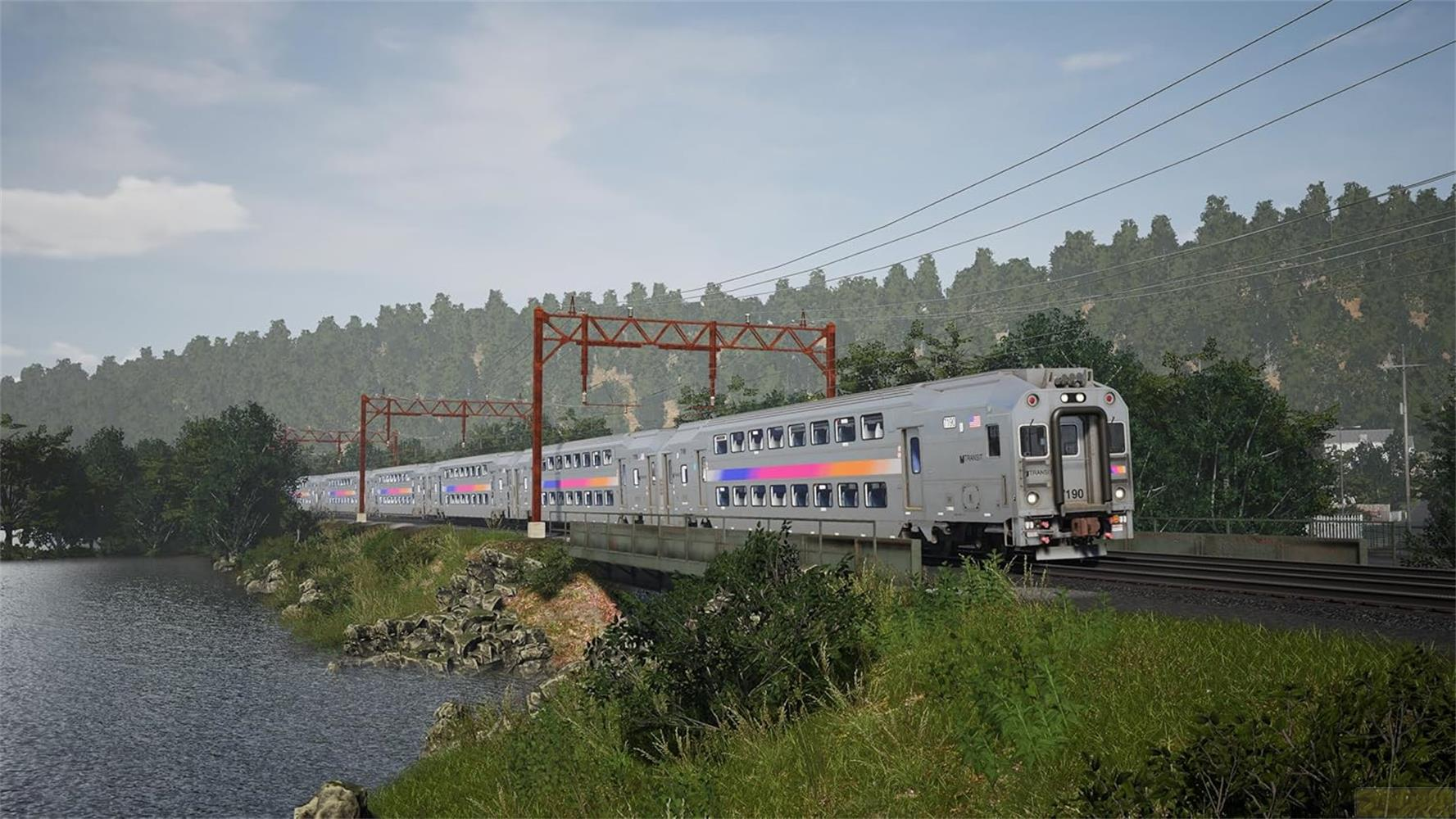 Un treno grigio con strisce colorate viaggia su un ponte sopra un lago, circondato da alberi.
