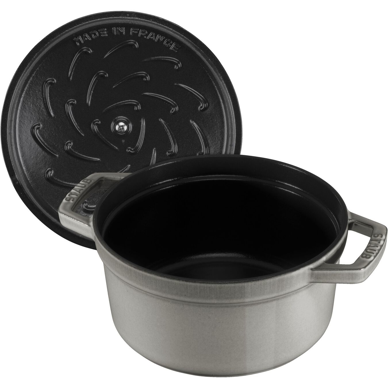 Olla Staub gris con su tapa negra abierta apoyada de lado.