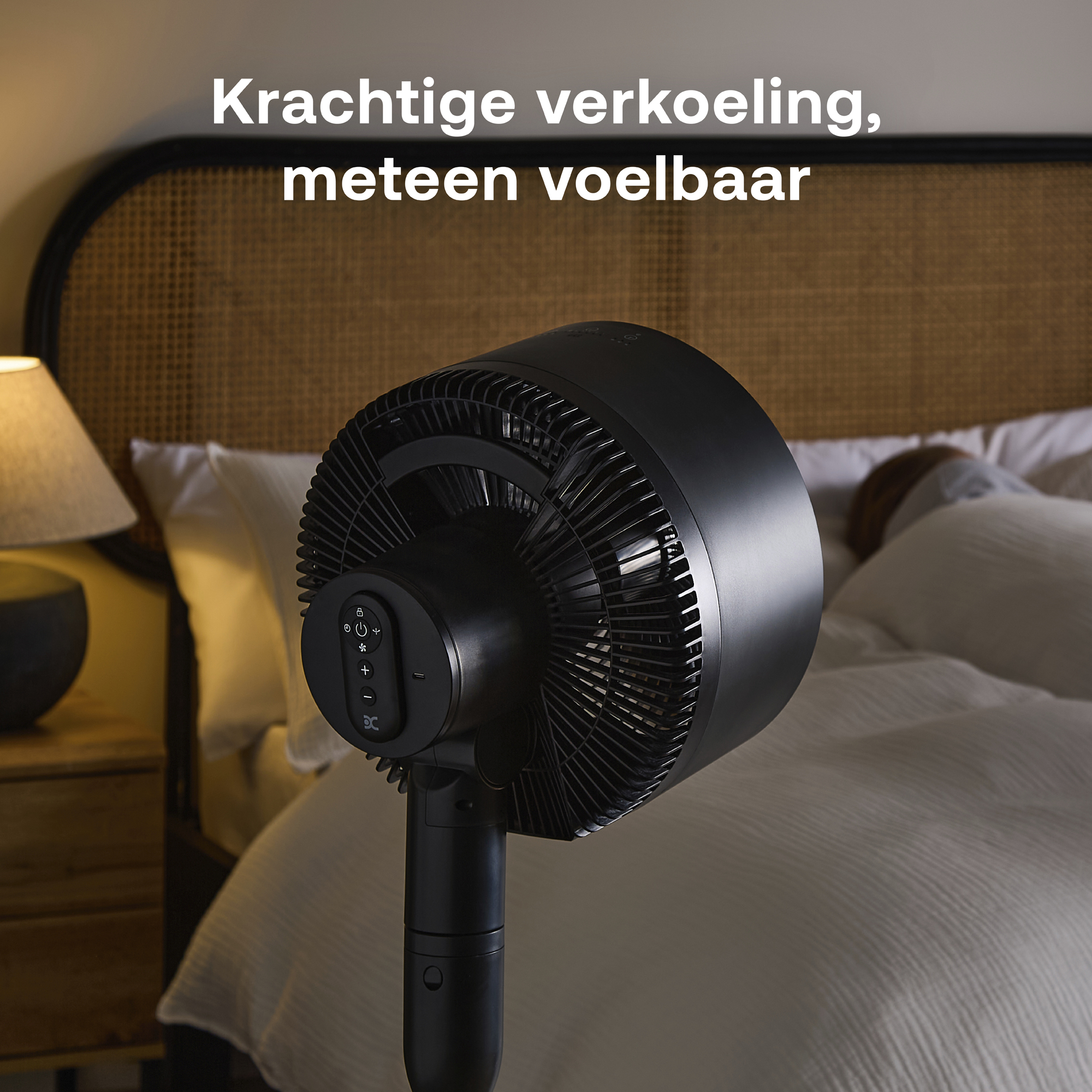 Een zwarte ventilator staat in een slaapkamer naast een bed.