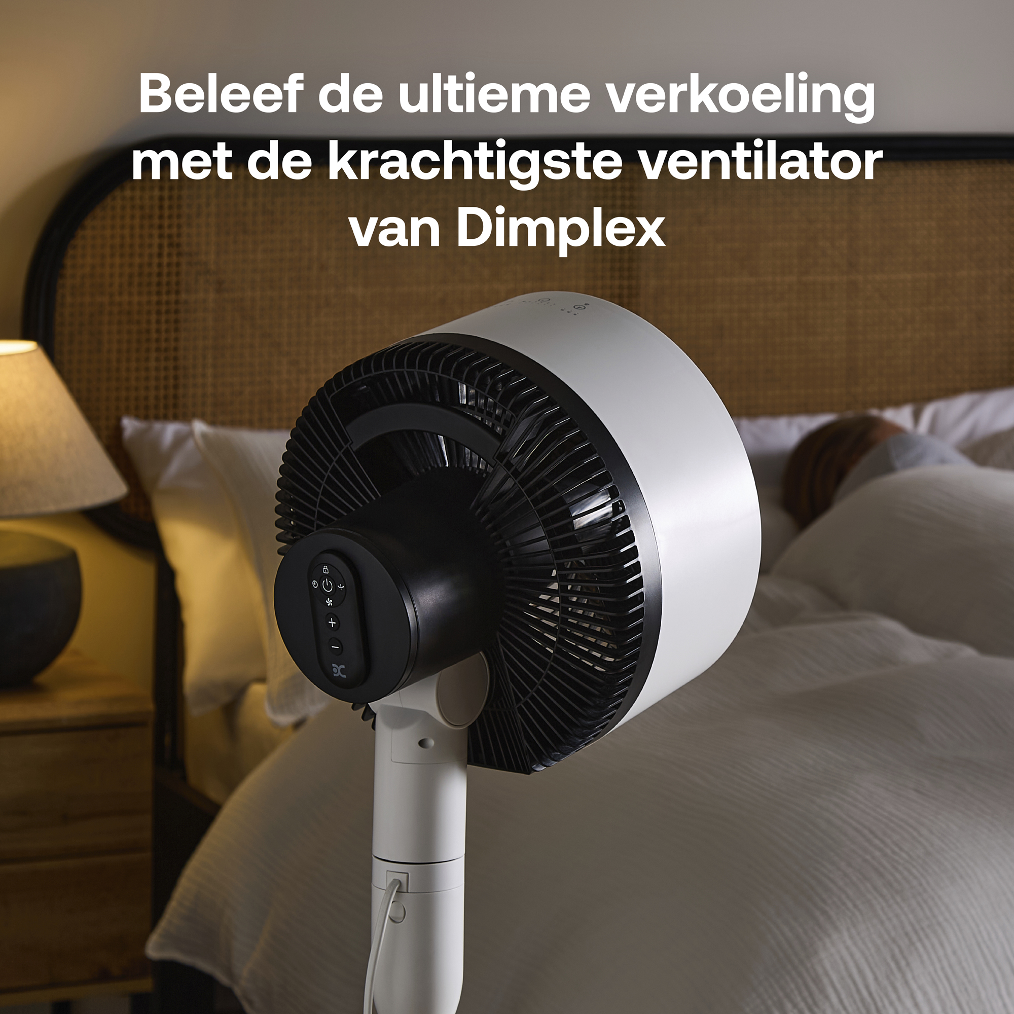 Een witte Dimplex ventilator staat naast een bed waar iemand slaapt.