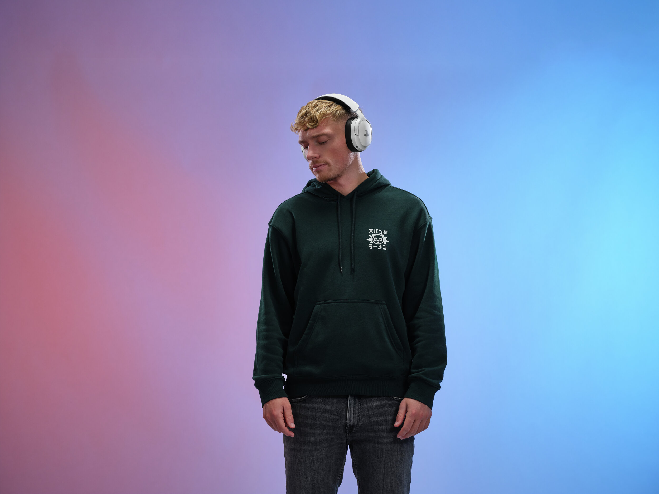 Een man met blond haar en koptelefoon draagt een donkergroene hoodie en jeans.