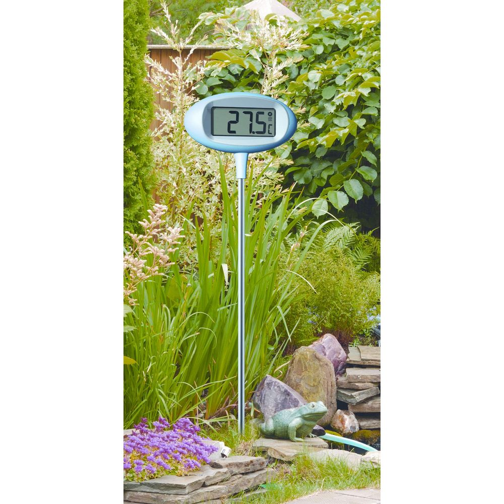 Ein Garten-Thermometer zeigt 27,5 Grad an, umgeben von Grün und Steinen.