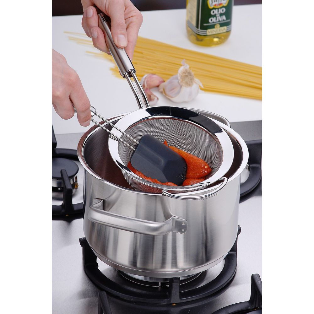 Ręce odsączają sos pomidorowy z sitka do garnka na kuchence. W pobliżu spaghetti, czosnek i oliwa z oliwek.