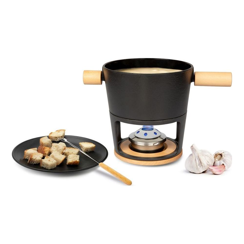 Une marmite à fondue noire avec poignées en bois repose sur un support avec un brûleur. Des cubes de pain sur une assiette.