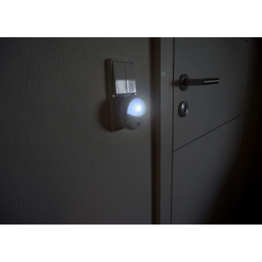 A small, round night light glows next to a light switch on a wall beside a door.