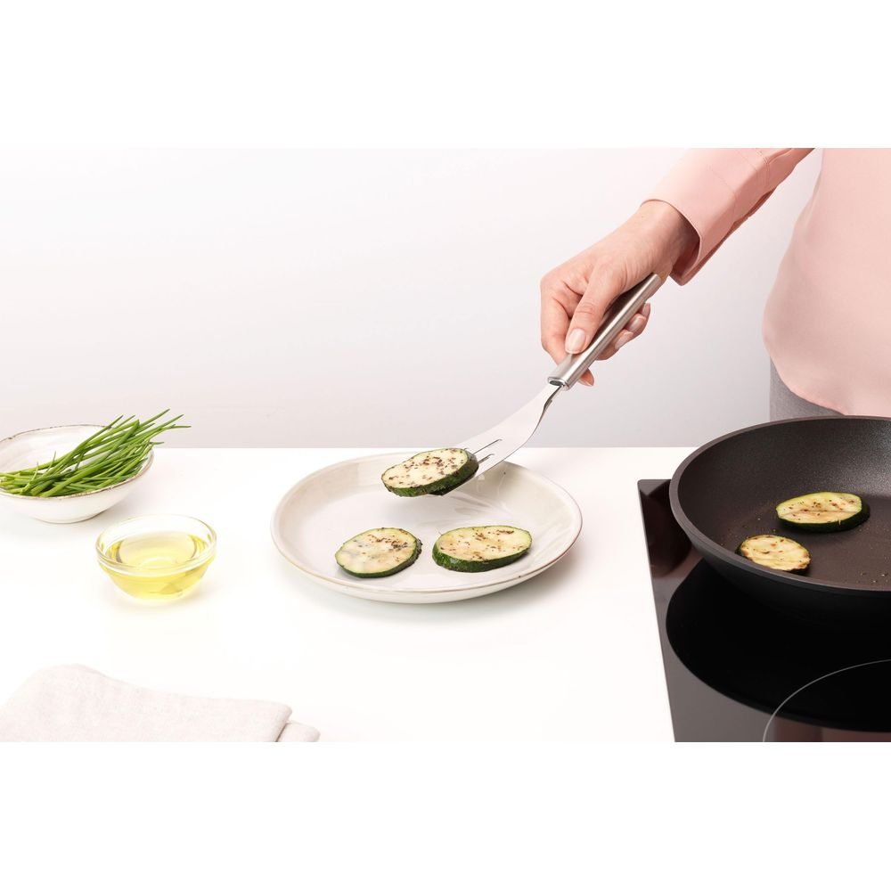 Fette di zucchine vengono messe su un piatto con una forchetta, accanto a olio e erba cipollina.