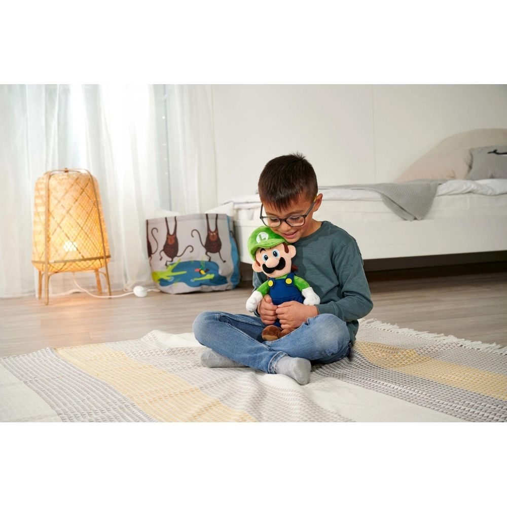 Ein Junge sitzt auf einem Teppich und hält eine Luigi-Puppe. Eine Lampe steht links.