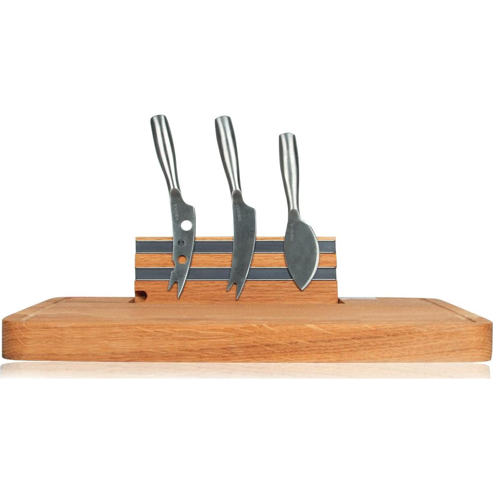 Three cheese knives with metal handles sit in a wooden block on a wooden cutting board.
