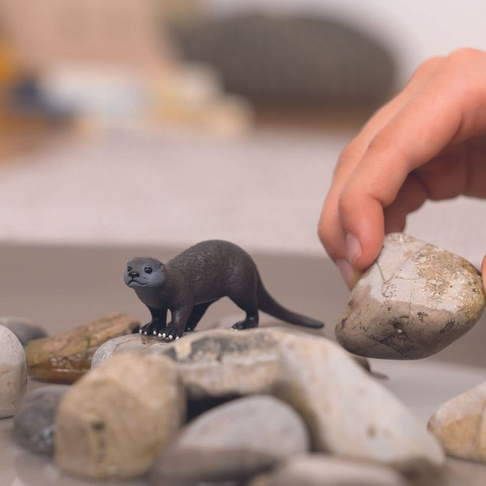 Ein Kind legt einen Stein auf Kieselsteine neben eine Otterfigur.