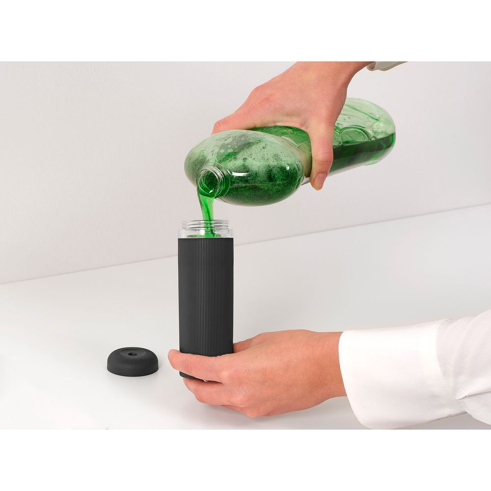 Grüne Flüssigkeit wird aus einer Flasche in einen schwarzen Behälter gegossen.