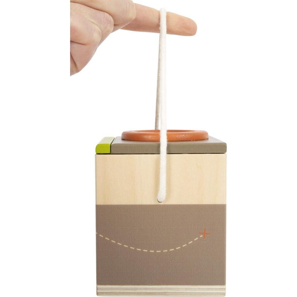 Un dito tiene una corda bianca attaccata a un giocattolo di legno con un anello arancione.