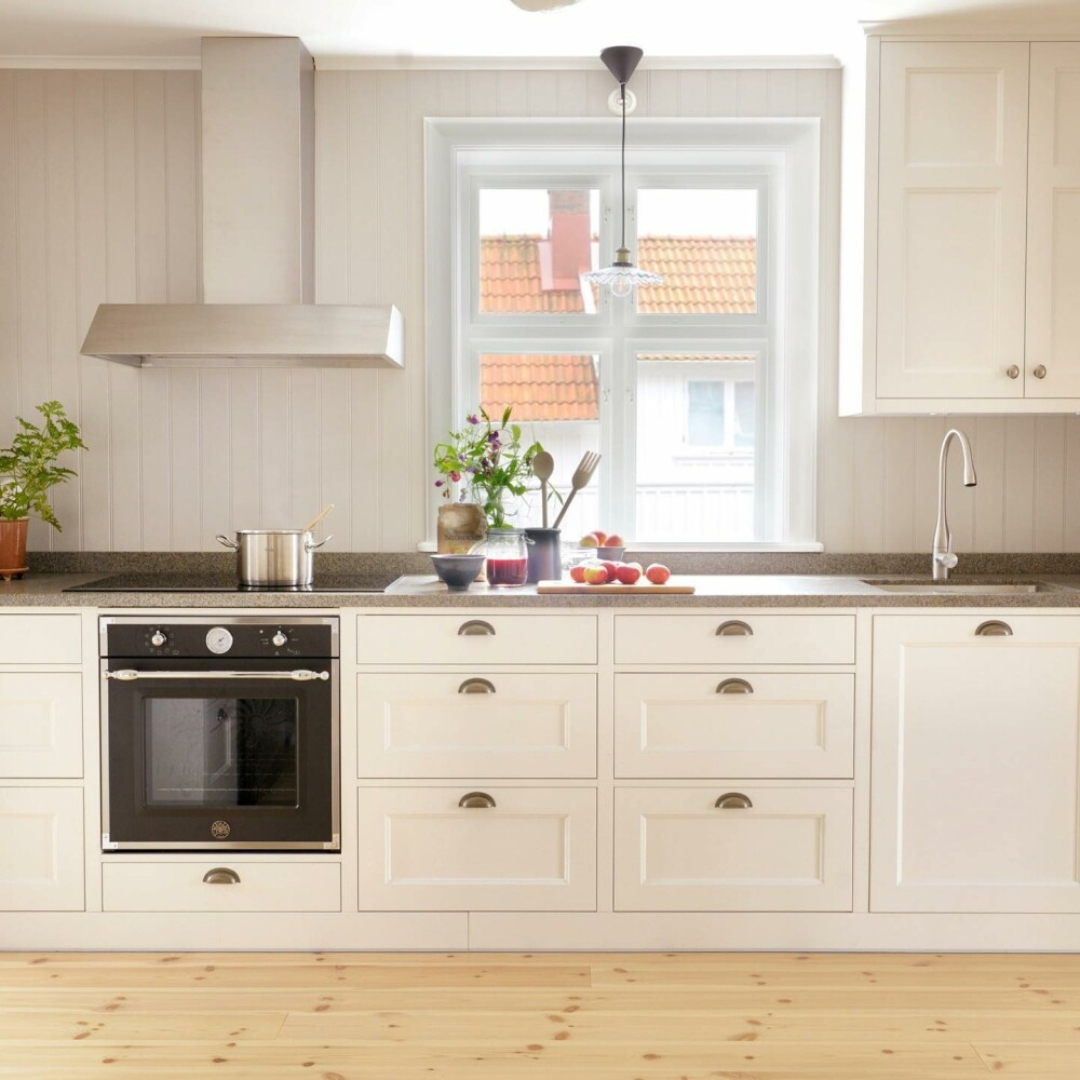Una cucina bianca con pavimenti in legno, un fornello, cassetti e una finestra.
