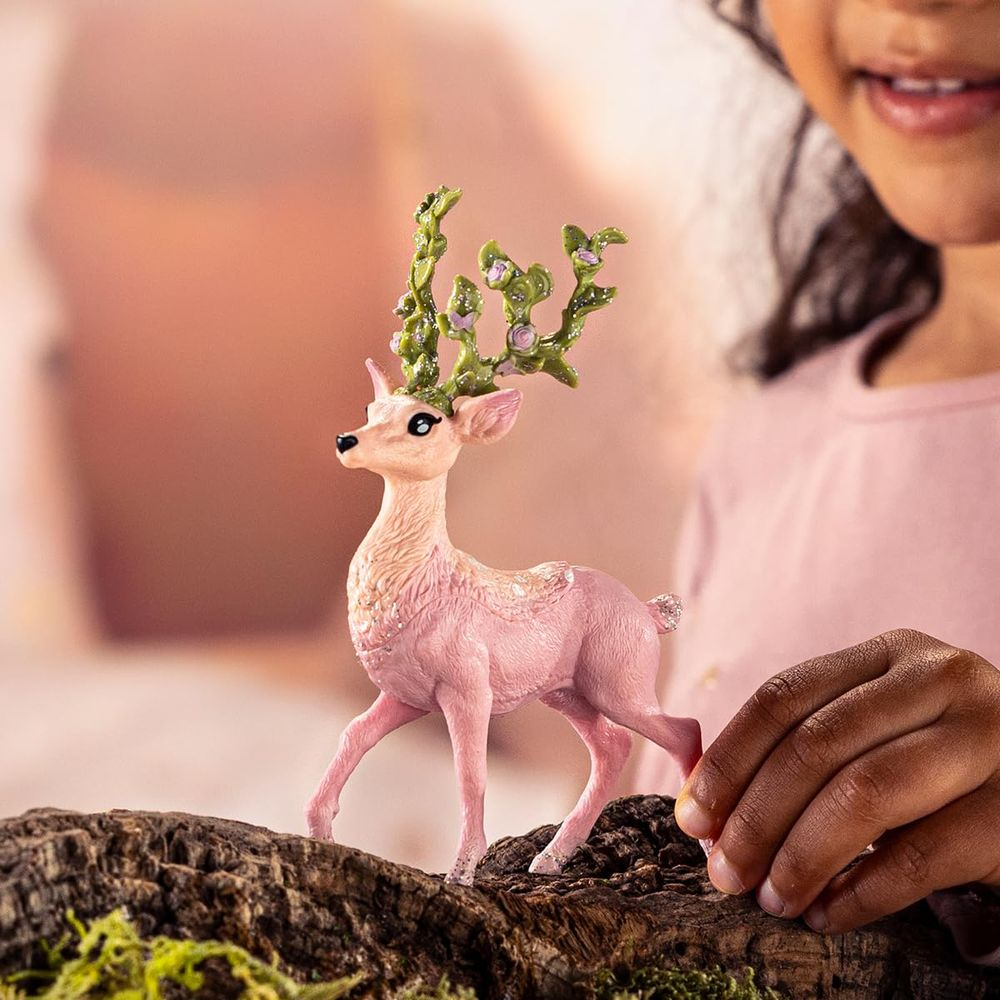 Un cervo rosa con corna verdi sta su un ramo. Un bambino lo tiene.