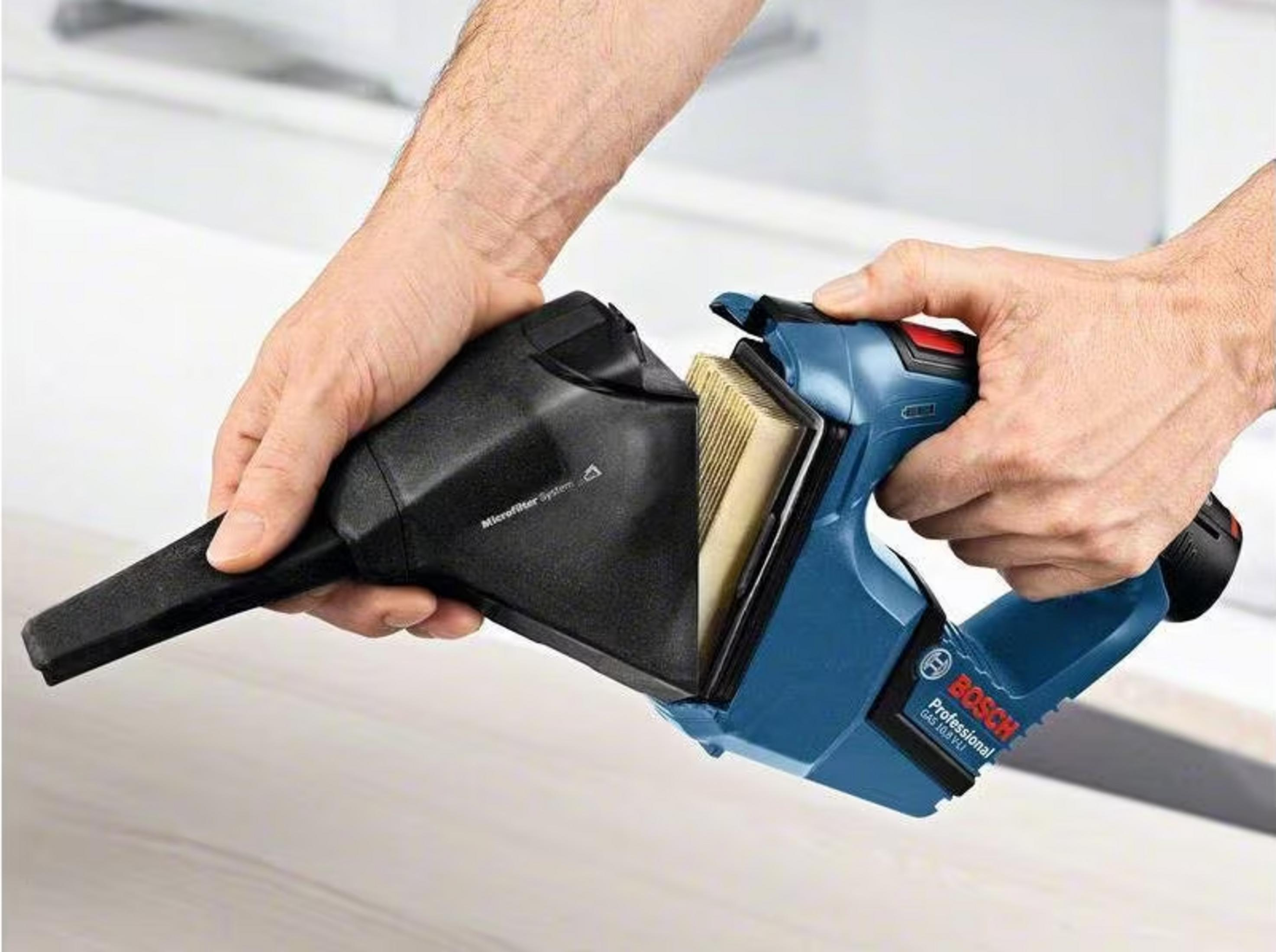 Hombre sujetando aspiradora inalámbrica Bosch azul con depósito y filtro extraídos.