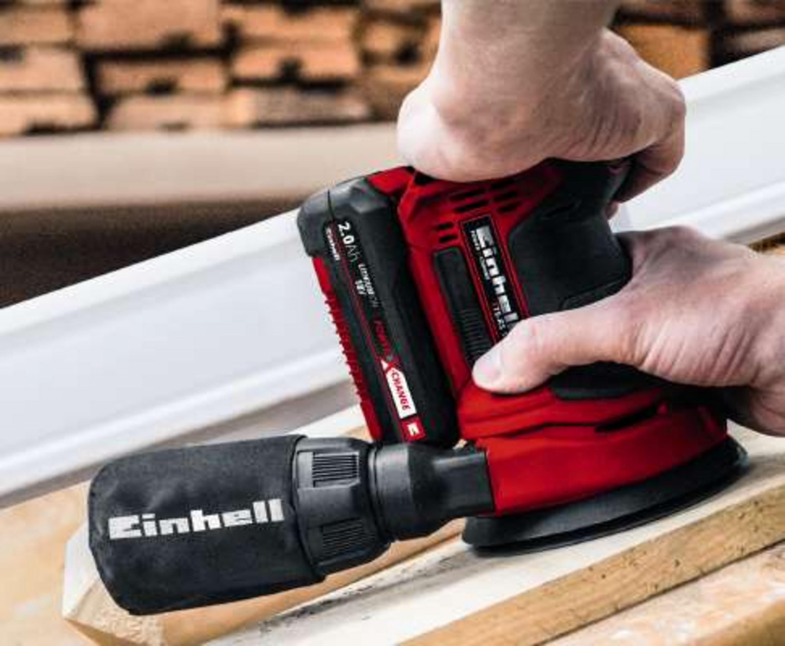 Un uomo leviga un pezzo di legno con una levigatrice orbitale rossa, sacco polvere.