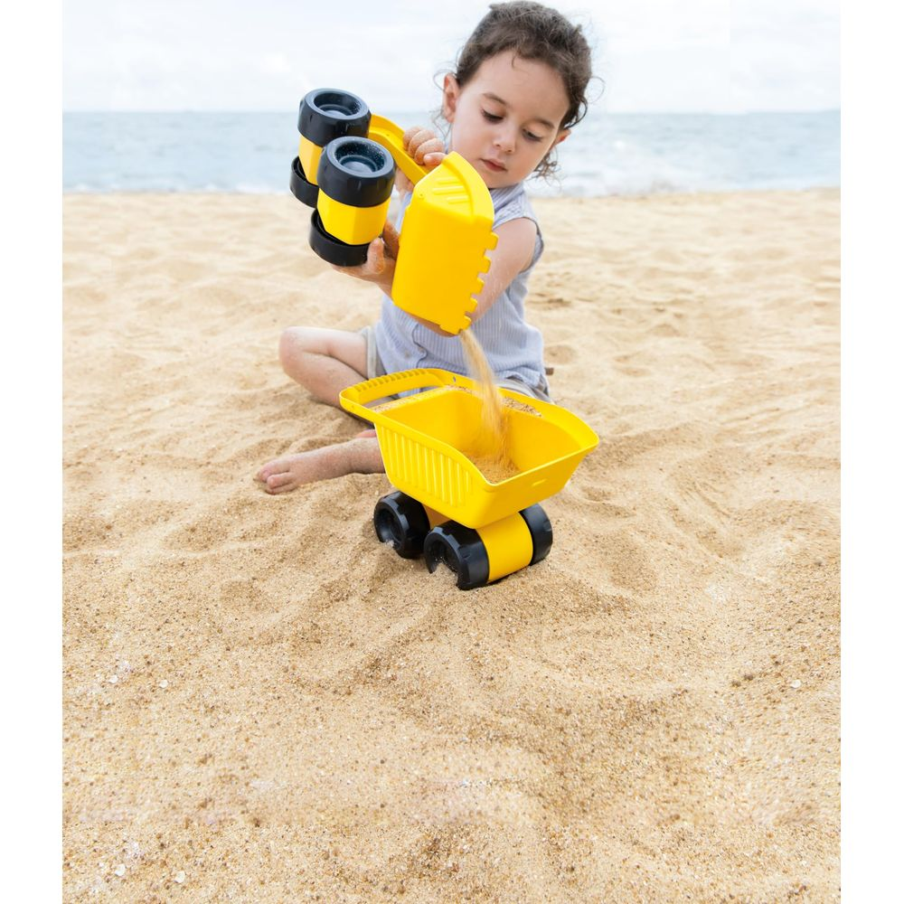 Una bambina gioca sulla spiaggia con giochi di sabbia gialli, versando sabbia in un camion.