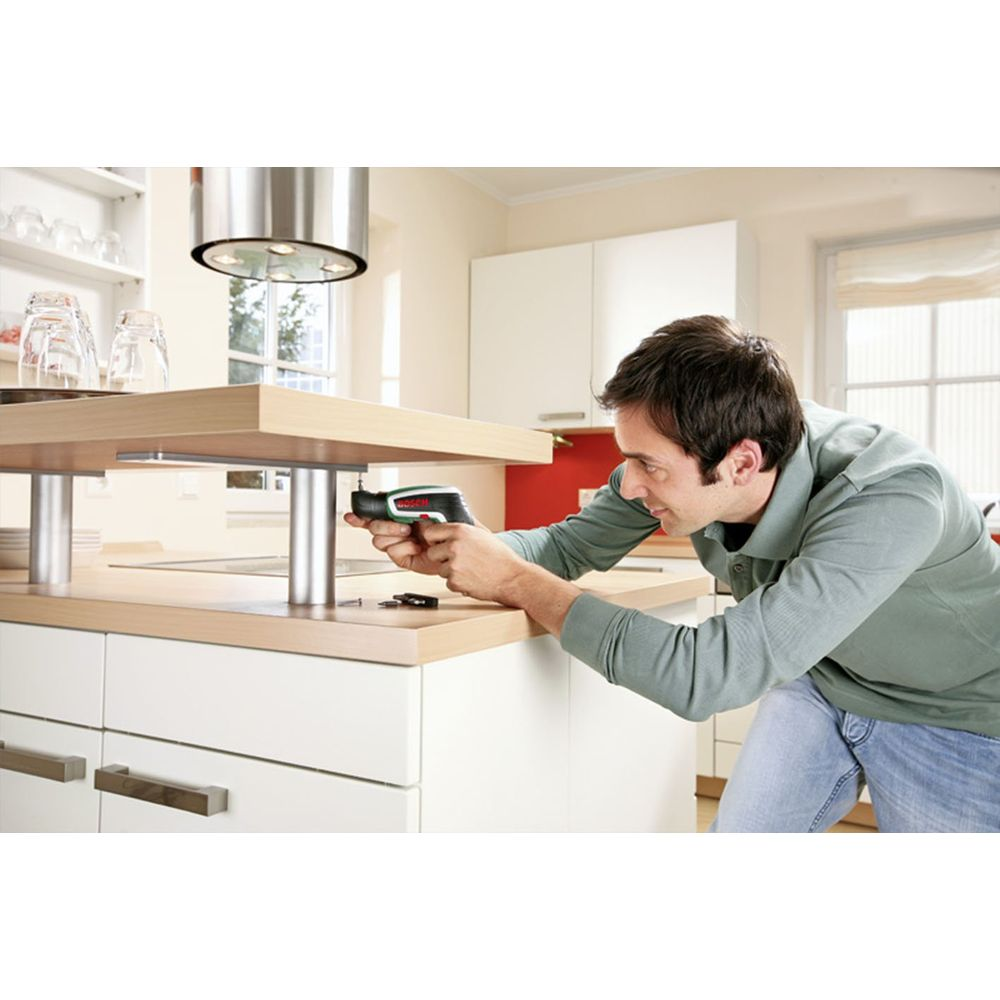Homme visse dans îlot de cuisine avec perceuse. Aménagement moderne.