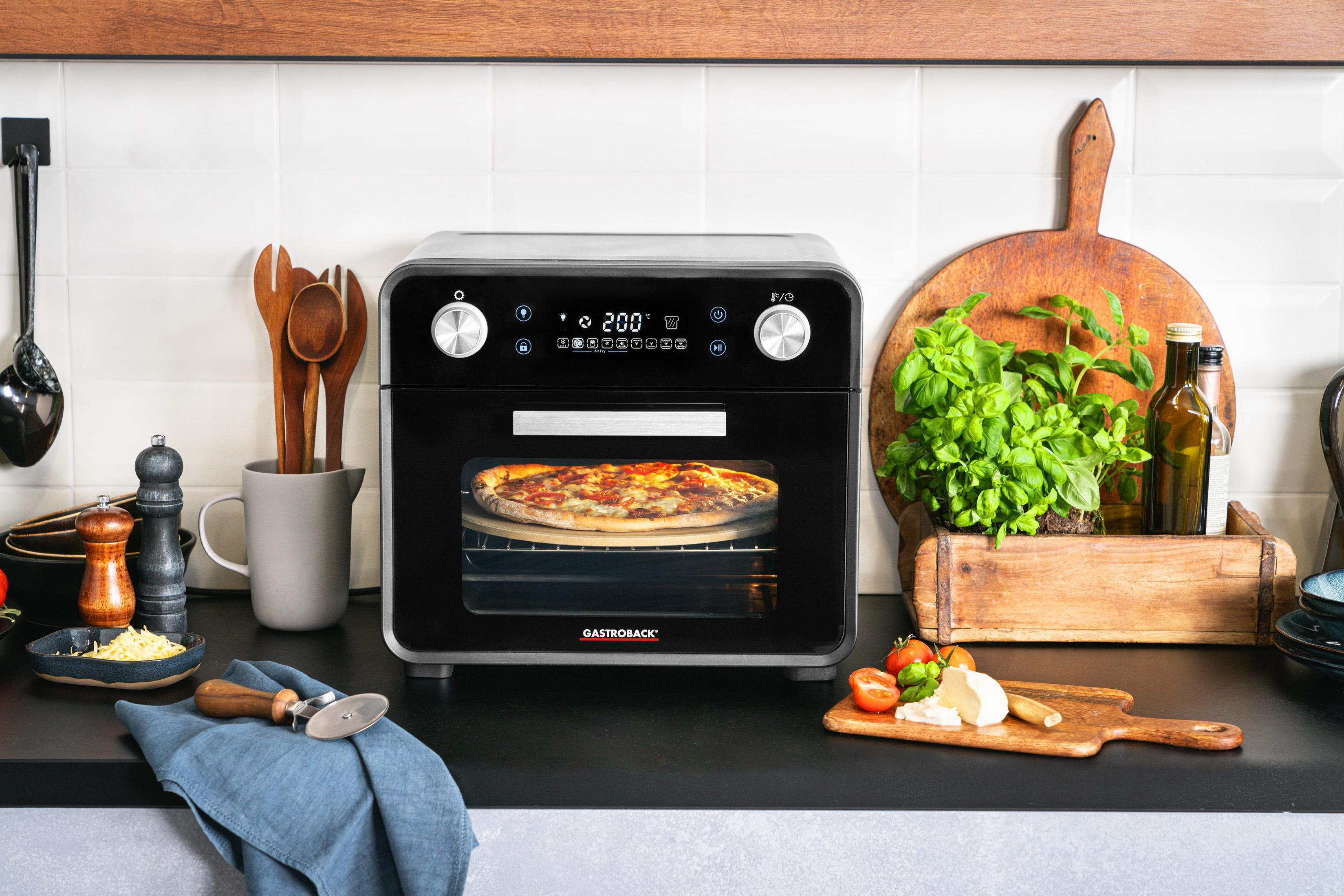 Czarny piekarnik z pizzą, obok świeże zioła i pomidory.