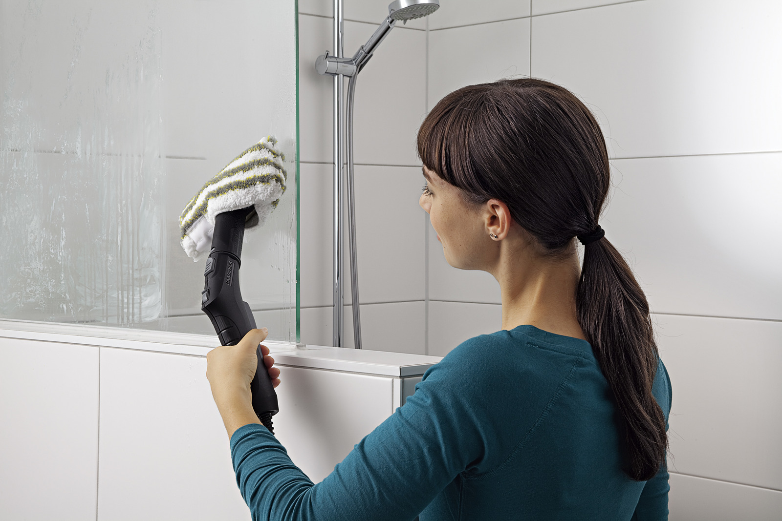 Frau reinigt mit Dampfreiniger eine Glasduschwand in einem Badezimmer.