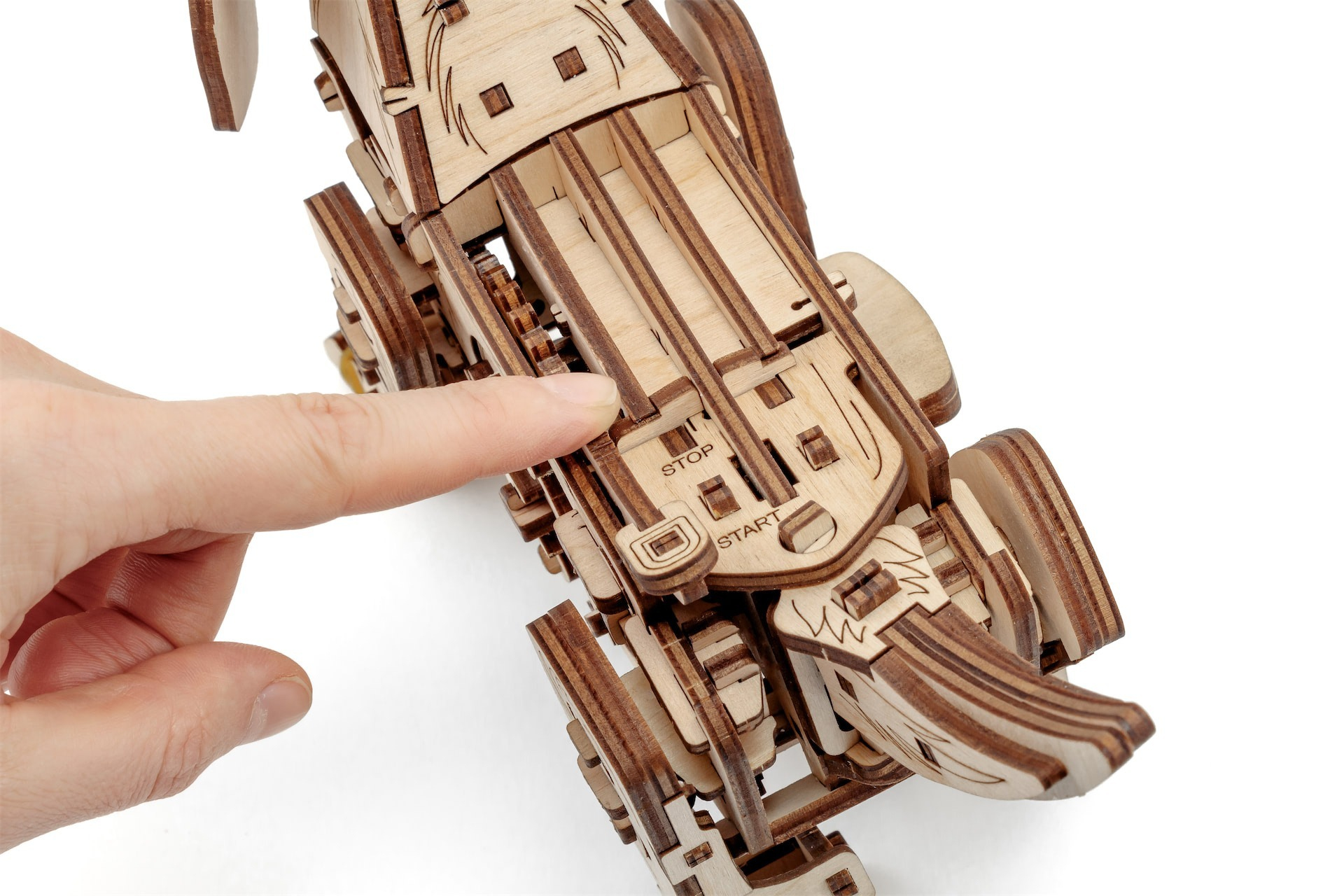 Eine Hand berührt ein Holzmodell eines Fahrzeugs mit Zahnrädern.